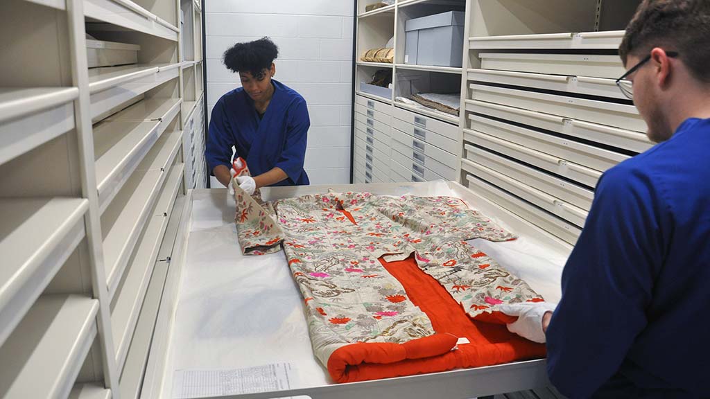 Two students arrange a kimono in a drawer on top of other textiles